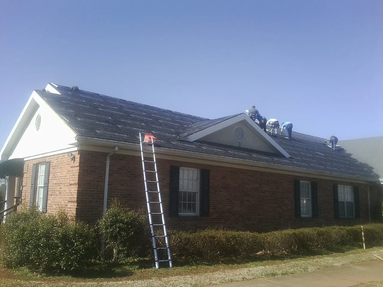 Crew tearing shingles off a brick ranch roof with a ladder set — Emergency Roof Repair work by our crew in Hamden